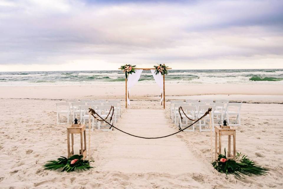 beach wedding ceremony with vintage lanterns on either side of the aisle and floral wooden arch at the altar