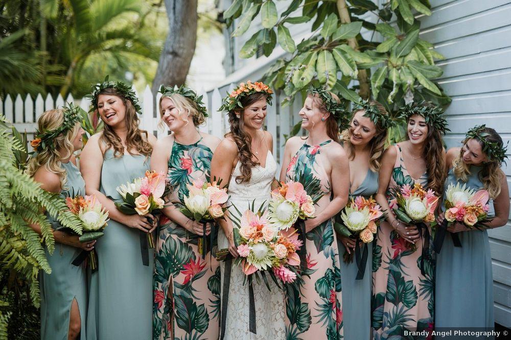 Bride wearing wedding gown in the middle of bridesmaids wearing alternating tropical-print and blue dresses