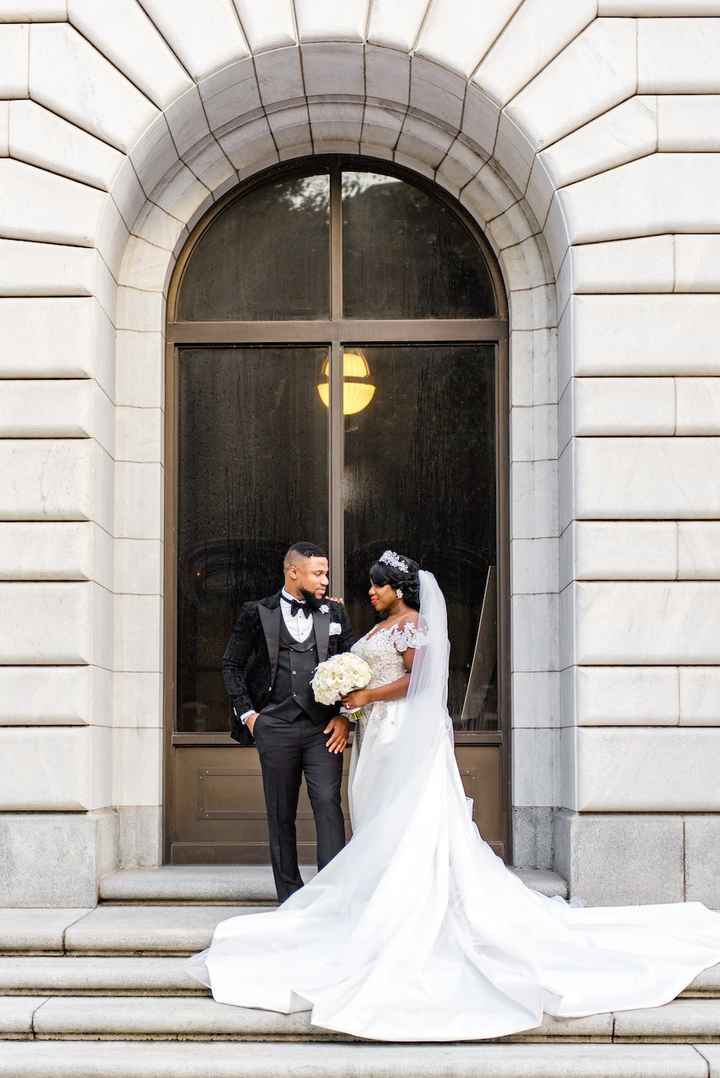 couple standing on steps under arch, black tux, white wedding dress with long train