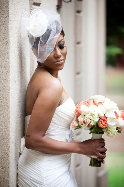 bride wearing a blusher against wall holding a bouquet 