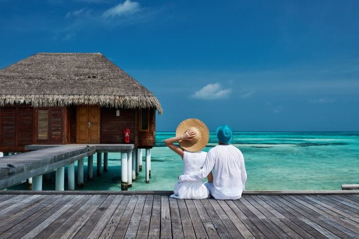 couple sitting on boardwalk in maldives looking at the ocean wearing hats by bungola