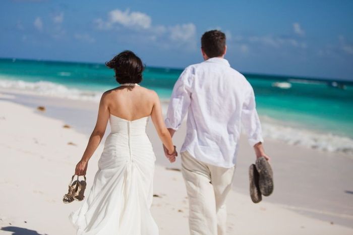 Couple walking hand in hand on beach with shoes off