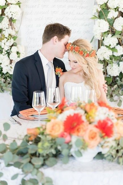 Couple at sweetheart table with bright orange and pastel flowers