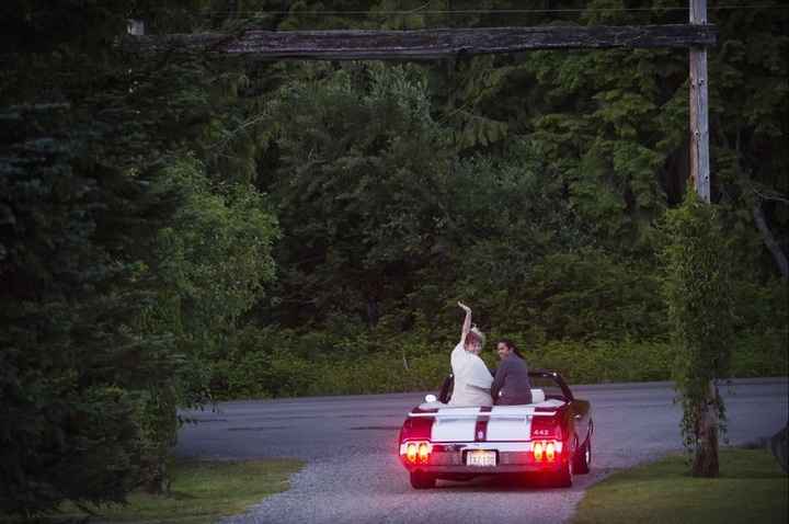 Recently married couple drives of in black convertible with two white racing stripes