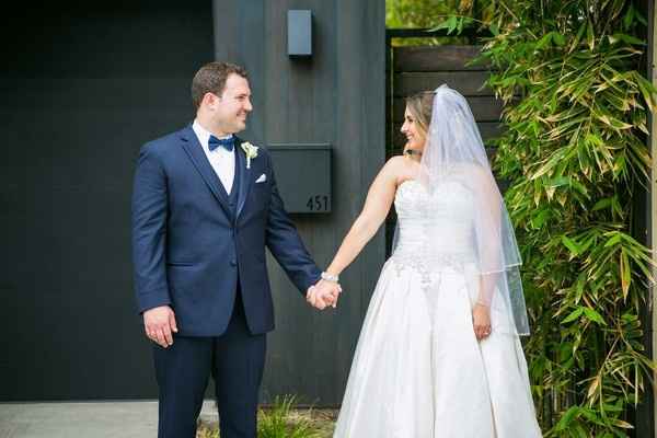 Groom in navy tux and bride in white gown and veil holding hands
