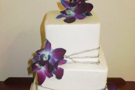 3-tier square cakes finished in white buttercream with silver striping.  Fresh purple dendrobium orchids accent the corners and top of this cake.