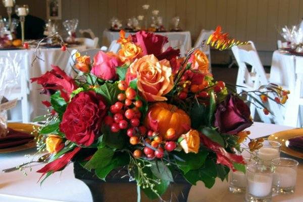 Festive fall centerpiece featuring roses, pumpkins, fall leaves, and other seasonal flowers