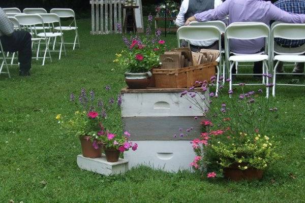 A Stack of Bee-Keeping Boxes topped with a vintage basket  hold the programs for this Outdoor Wedding Ceremony. all items available for rent.