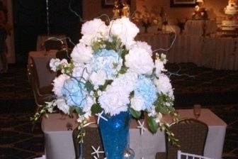 Tall glass vase (rental) with tiffany blue gell and lights. Large arrangement on top of hydrangea, roses, peonies,etc. Hanging globe votives and white starfish