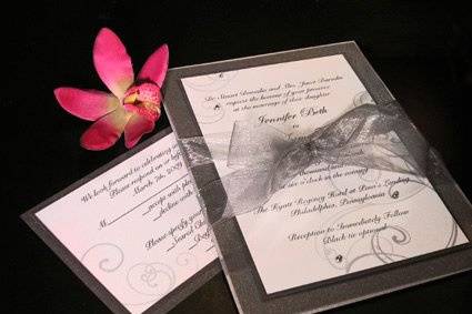 Custom wedding invitation in white and charcoal with swirl design and silver ball accents. Tied with a sheer platinum ribbon bow.