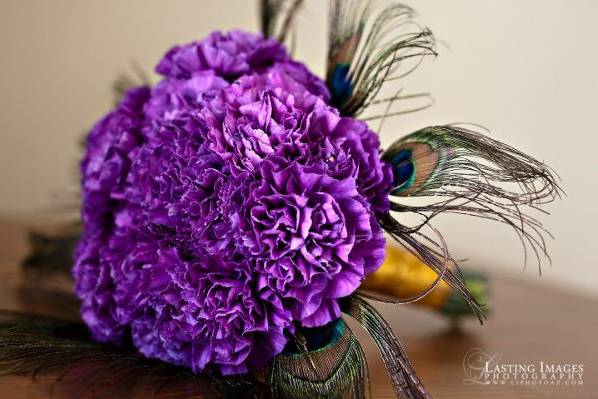 Bridal bouquet of deep purple Moonglow carnations and peacock feathers with a gold satin wrap.