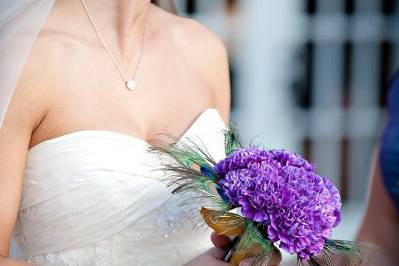 Bridal bouquet using deep purple Moonglow carnations and peacock feathers is a pop of color against the bride's dress