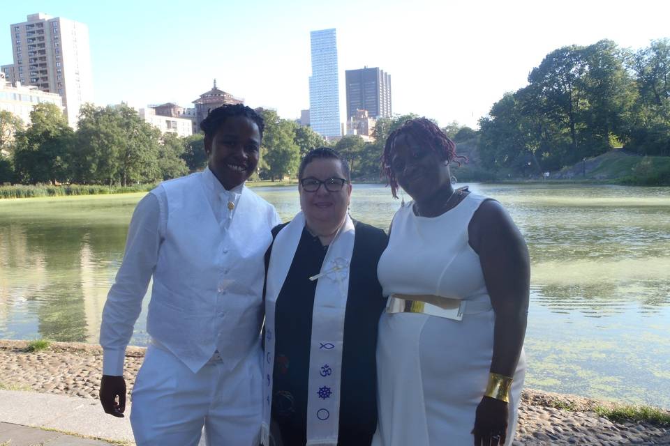 Divine summer wedding at Central Park Harlem Meer with lake in background. Space blessing with incense done by one of the brides to prepare the space for ceremony. Harp music played. Ritual: Jumping the Broom.