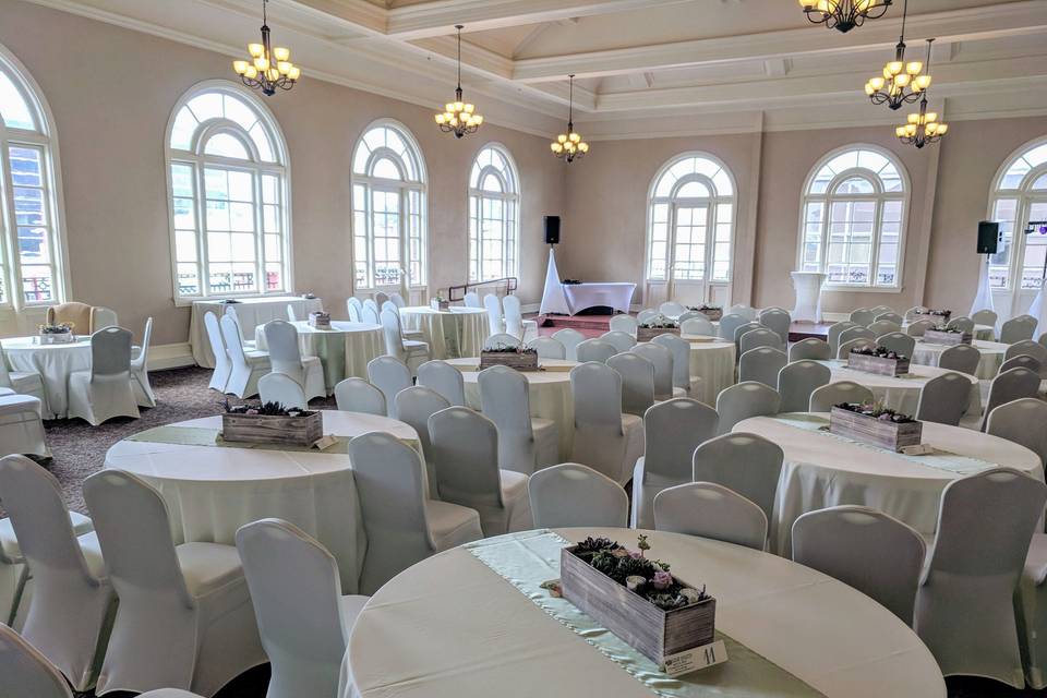 Ballroom with ivory chair covers (available for rent). Set up for guests to be seated at tables for the ceremony