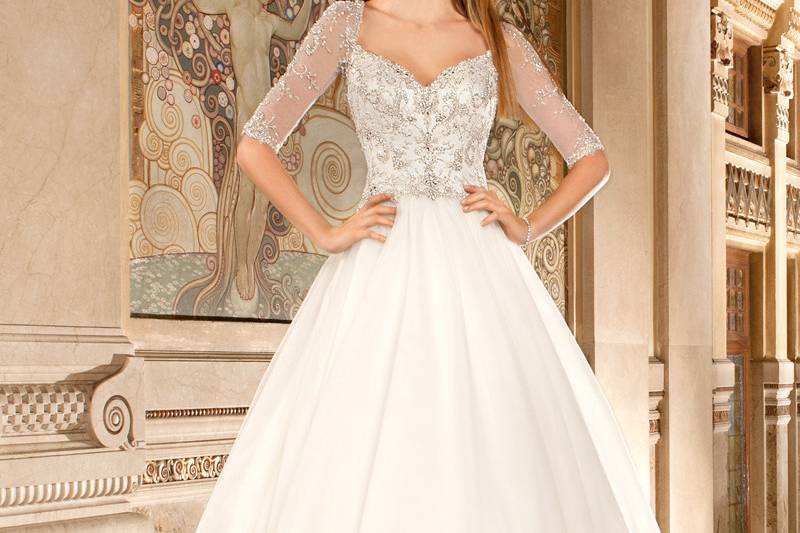 565This classic tulle ball gown features a heavily beaded embroidered bodice accented with crystal beading, sheer beaded ¾ length sleeves and a deep illusion back with button closure. Gown is finished with a chapel train.