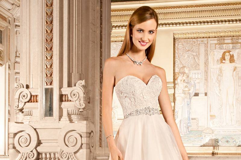 1479This elegant, strapless gown with sweetheart neckline features a tulle, a-line skirt with a jeweled belt on the natural waist. The bodice and hem are adorned with embroidered lace that continues into the chapel train.