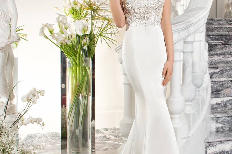 221This elegant, luxe satin, form fitting gown features a unique design of beaded embroidery and jewel encrusted three-dimensional flowers on the bodice and throughout the dramatic illusion back with button closure.