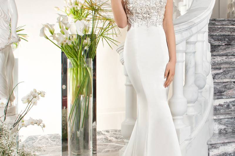 220This elaborately embellished fit n flare gown with multi-feathered skirt features a sweetheart neckline with sheer beaded cap sleeves flowing into a plunging low back.