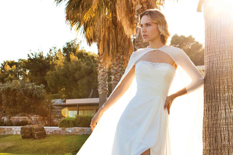 201Chiffon Strapless, A-line destination wedding gown with a ruched, wrap bodice, beading on neckline, and Chiffon cape. The skirt on this bridal dress features a high side slit and Chapel Train.