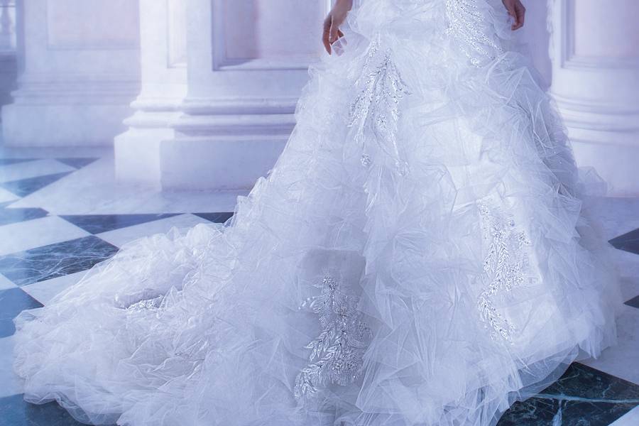258Tulle, A-line wedding gown with shimmering beaded lace embroidery, high sheer neck, ¾ length sleeves and ruffles with sprays of beading on skirt. The high sheer back on this bridal dress features buttons and ruffled, attached train.