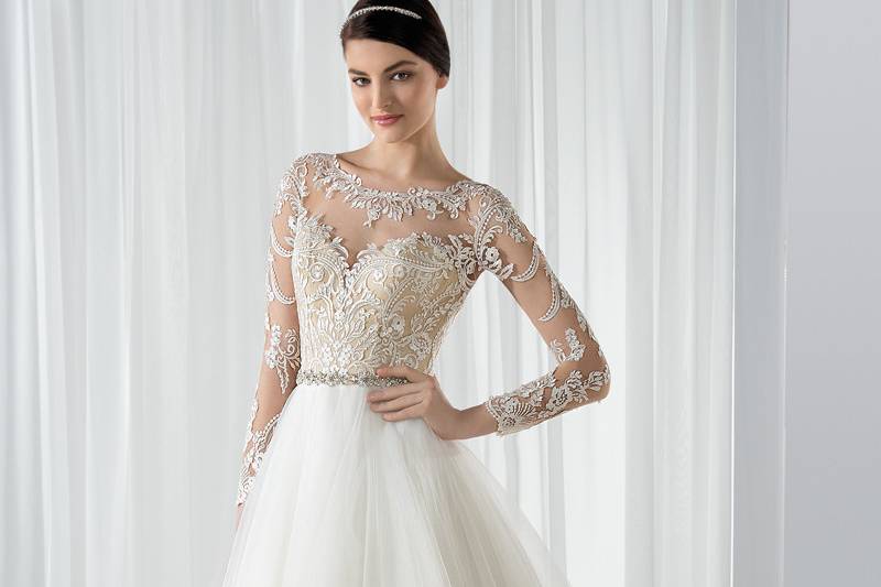 Style 591 <br> This timeless Tulle, Ball Gown with jeweled trim on waist features delicate lace appliques on the natural illusion back, neckline and long sleeves.  The back features jeweled button closures and Chapel train.