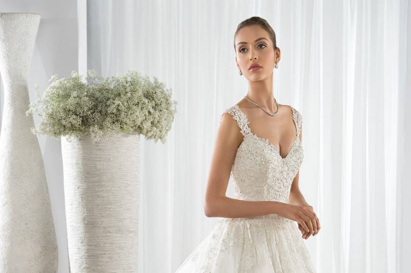 Style 606 <br> This shimmering beaded tulle Fit-N-Flare gown with a V-neckline, features beaded straps that transition into a sheer illusion back with buttons.  The striking beaded embroidery cascades from the bodice into the tulle skirt with sparkling underlay and flows into the Chapel length train.