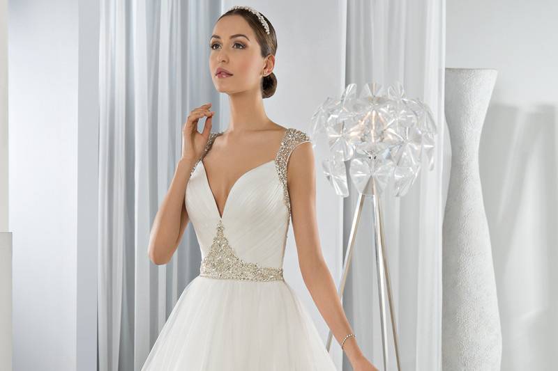 Style 607 <br> This dreamy Tulle Ball Gown with plunging V-neckline is embellished with crystal jeweling on the waist.  The sheer beaded cap sleeves transition into a magnificent jewel embellished low sheer back with button closure.  The back features a Chapel length train.