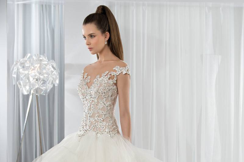 Style 611 <br> This unique Tulle Ball Gown with dropped waist features an intricate design of embroidered lace with beading and natural sheer neckline transitioning into a dramatic low back.  The extravagant multi-tiered Tulle skirt flows into a Chapel train.