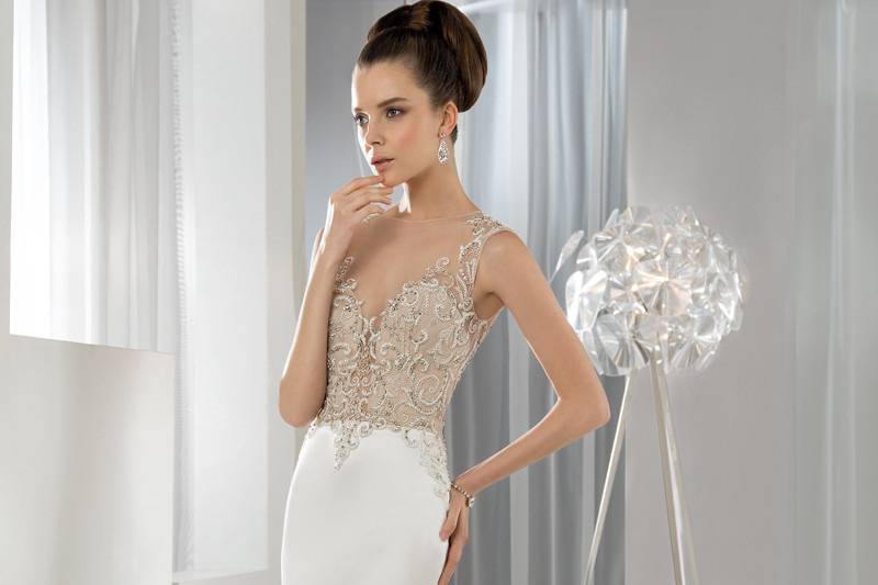 Style 612 <br> This sophisticated sleeveless, Lux Satin, Fit-N-Flare gown features crystal embellished embroidery  on the bodice with natural sheer high round neckline flowing into a dramatic, low sheer back with button closure.  The satin skirt flows into a Chapel length train.