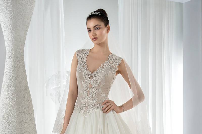 Style 634 <br> This glamorous Fit-N-Flare gown features an organza- layered skirt and beaded bodice with a high neckline. The beaded cap sleeves transition to a low dramatic back embellished with button closure and an extravagant layered Chapel train.