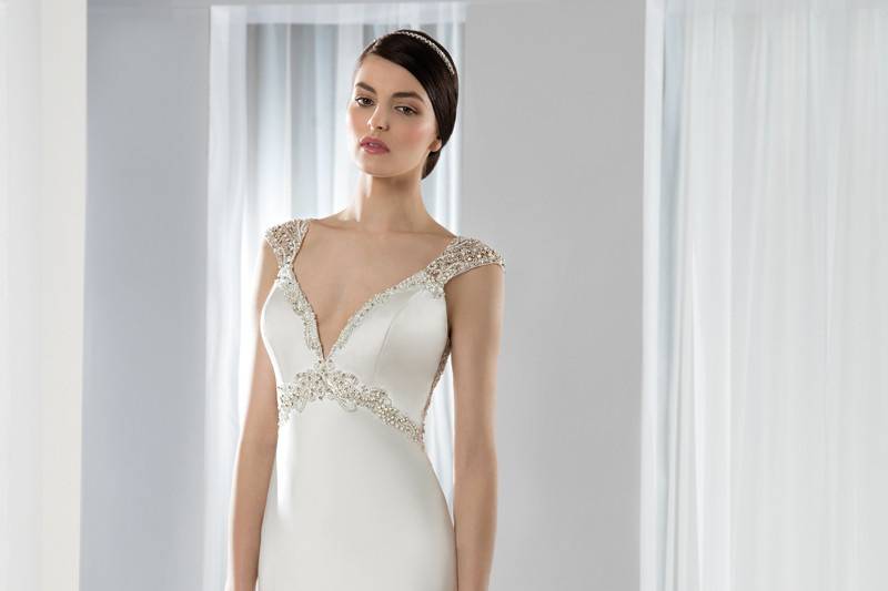 Style 637 <br> This timeless luxe satin Sheath gown features a plunging V- neckline, beaded empire waist, neckline and cap sleeves. The beaded sheer back is embellished with button closure and a Chapel length train.