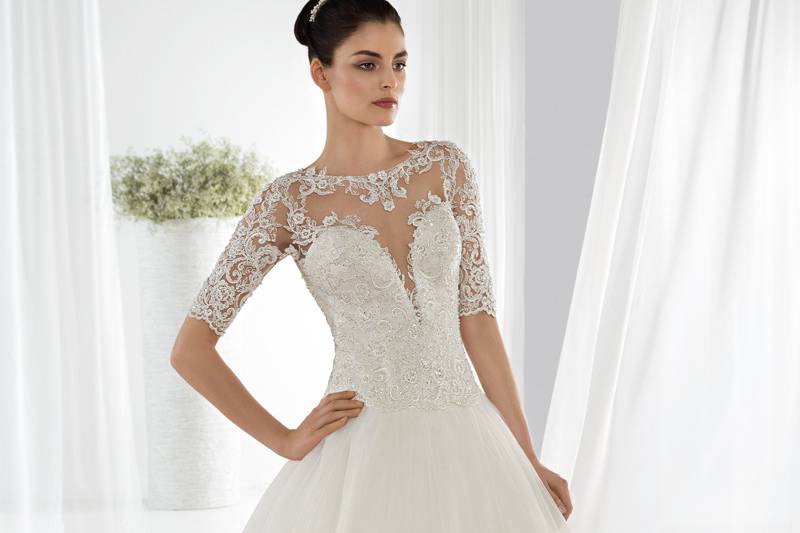 Style 644 <br> This Classic Ball Gown is embellished with a beaded lace bodice and tulle skirt, an illusion neckline and ¾ length sleeves. The back features a low open sheer back with lace appliques and an extravagant tiered Chapel train.