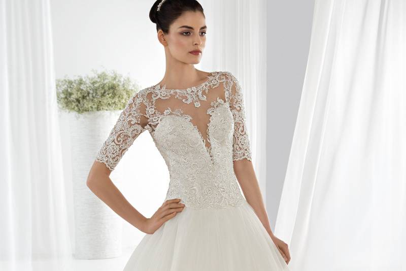 Style 654 <br> This unique Ball Gown features a ruffled beaded tulle skirt, beaded bodice with a sweetheart neckline and Basque waist. The sheer beaded cap sleeve transitions to a sheer open back embellished with button closures. The back features a Chapel train.