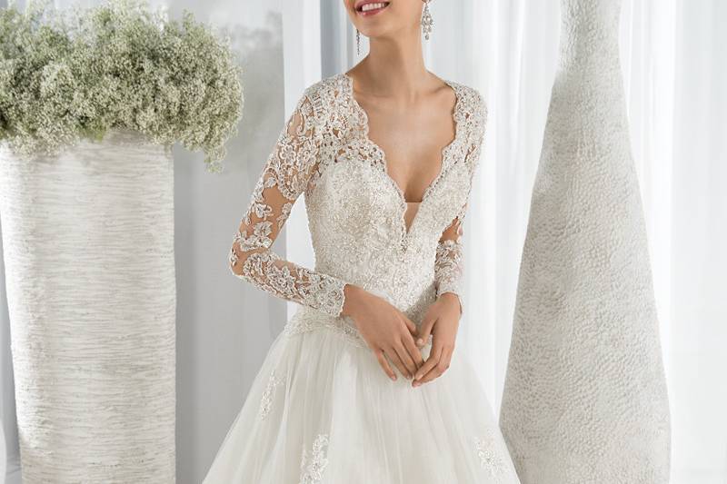 Style 646 <br> This dreamy Ball Gown features a plunging V- neckline with a beaded lace bodice and sheer lace long sleeves. The sheer open back is embellished with beaded lace and a Chapel train.