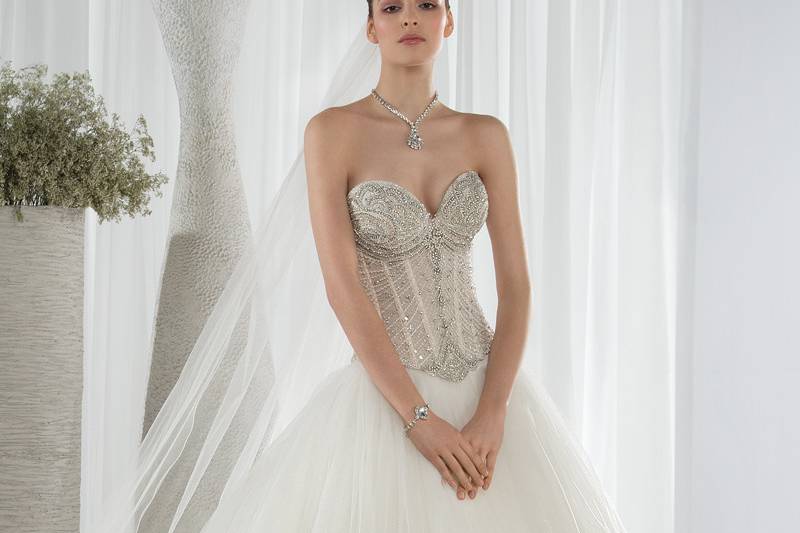 Style 647 <br> This glamorous Ball Gown is embellished with a beaded lace bodice with a sweetheart neckline and Basque waist. The tiered tulle layer skirt cascades into a Chapel train in the back. The back features a lace-up closure.