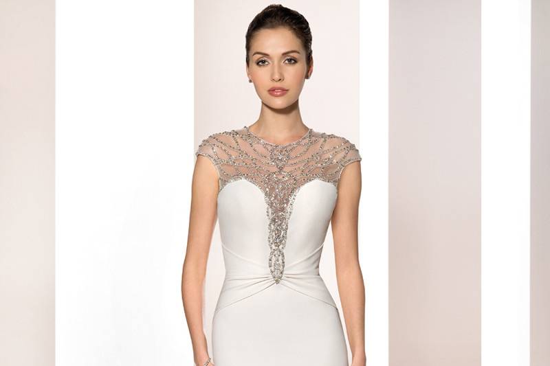 Style 698 <br>	Luxurious Crepe and shimmering beaded detailing over sheer illusion on the Bateau neckline create this glamorous sleeveless sheath gown with a dramatic keyhole back and draped Sweep train finished with beaded broach.