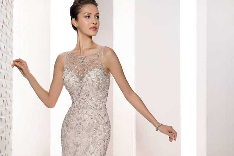 Style 696 <br>	This shimmering, sleeveless beaded tulle Sheath with Chapel train features intricate beaded embroidery over a Sweetheart neck silhouette.  The beaded illusion Bateau neckline flows into a stunning sheer beaded back with buttons.