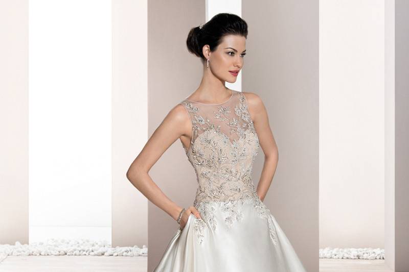 Style 692 <br>	This elegant sleeveless gown with Sweetheart neckline features a sheer overlay with decadent beaded embroidery flowing into a low sheer back with button closure.  The voluminous Satin A-line skirt features side box pleats and flows into a Chapel train.