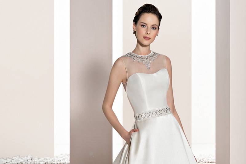 Style 691 <br>	Timeless elegance describes this sleeveless, Mikado A-line gown with crystal beaded belt and inverted box pleats that flow into a Chapel train.  The soft Sweetheart neckline features a sheer overlay with a jewel encrusted neckline.