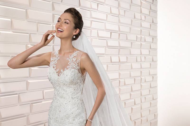 Style 677 <br>	Lace details adorn this striking sleeveless, sheath gown with sheer illusion neckline that transitions into an exquisite lace over sheer illusion back finished with buttons.  A Chapel train adds the finishing touch.