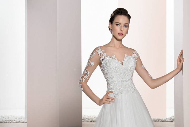 Style 676 <br>	Classic meets contemporary with this romantic Ball gown featuring Venice lace over barely there illusion sleeves and lace bodice that transitions into a low dramatic sheer back with covered buttons.  The tulle skirt flows into a Chapel length train.