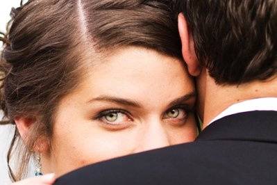 The bride looks into the camera lens with shining eyes as her new husband holds her close in this wedding photography session.