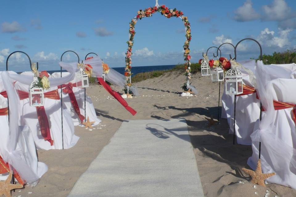 Coral color theme on arch, chair sashes & shephard hooks with lanterns