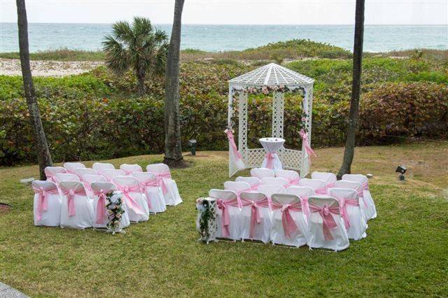 Light pink silk flowers on arch and pedestals in aisle. Sea Watch restaurant garden overlooking ocean.