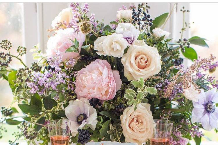 A lush centerpiece in a vintage-inspired silver mercury vase featuring peonies, anemone and sand colored roses.