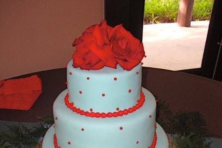 Teal and red fondant covered cake with small red dot accents and live roses and table decorations.