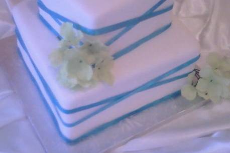 White square fondant covered wedding cake with teal criss cross ribbon and silver monogram cake top.
