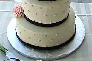 White buttercream 3 tier wedding cake with black ribbon and pink dot accents.  Live pink roses and monogram cake topper.