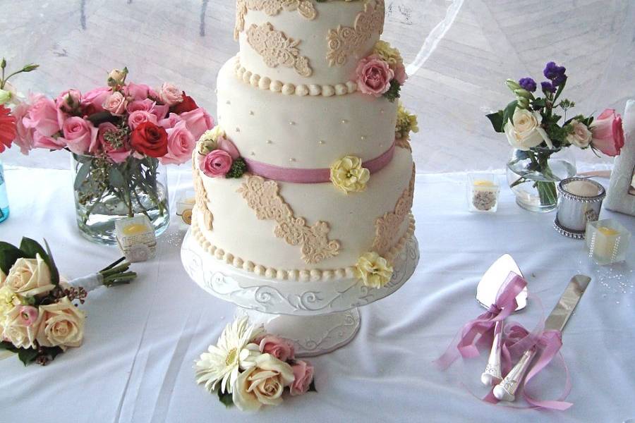 Round vintage lace wedding cake with pink and yellow roses.