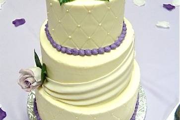 Buttercream cake with a fondant pleated sash, similar to the brides dress.  Purple piping and live roses.